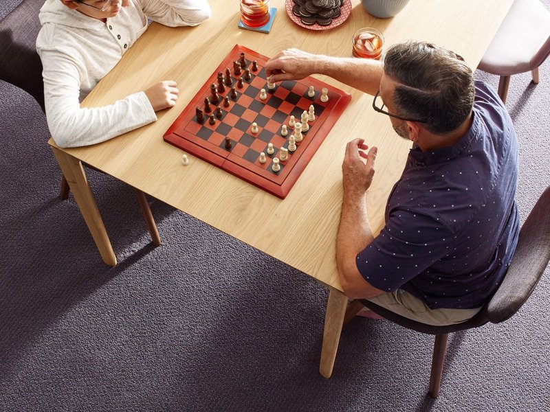 people playing chess at a wooden table in a room with purple carpet from Pritchett's Flooring Design Center in the Colonial Heights, VA area